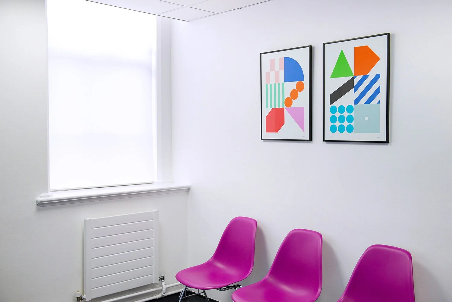 Framed geometric artworks above pink chairs