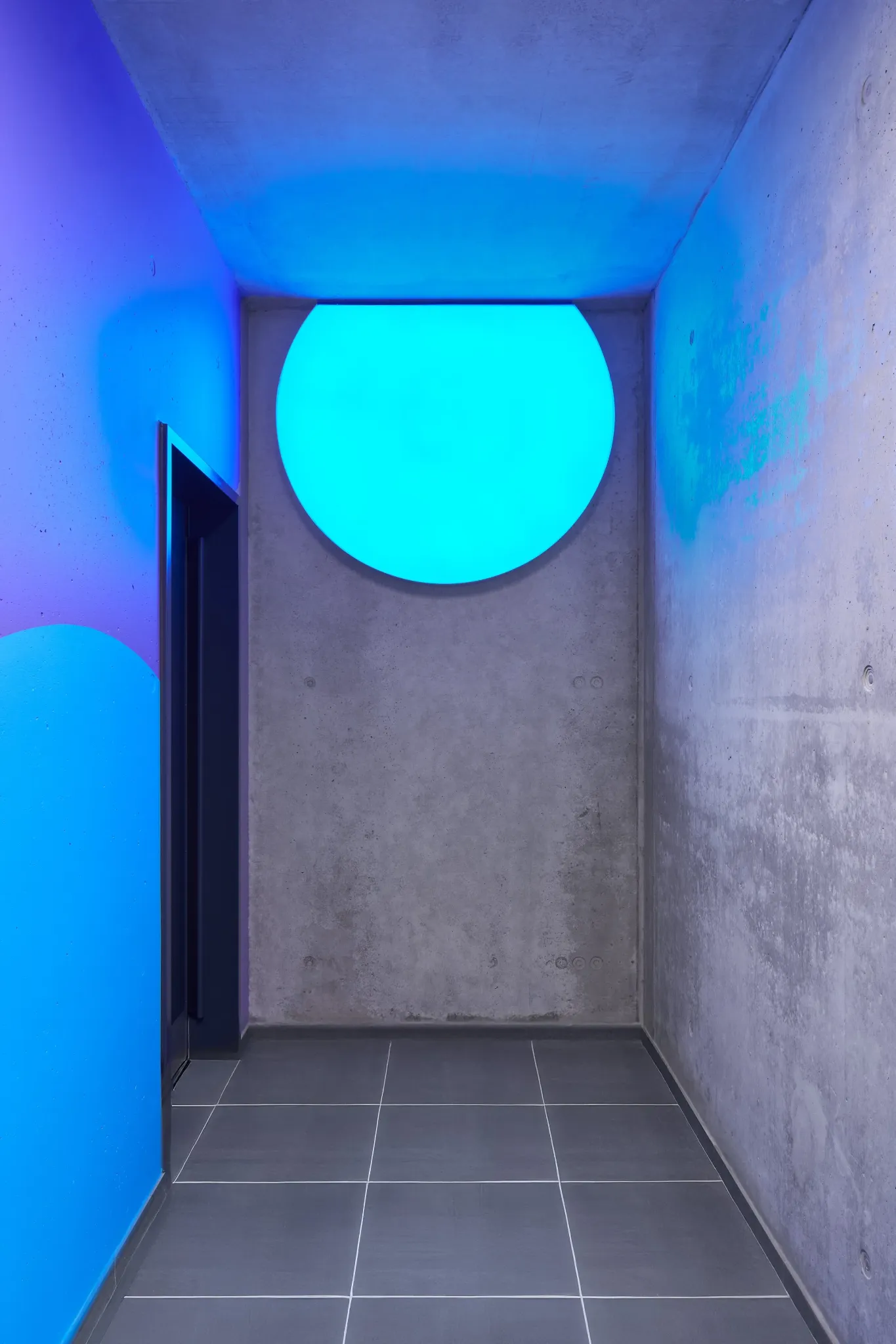 Illuminated blue circular landmark at the end of a concrete corridor