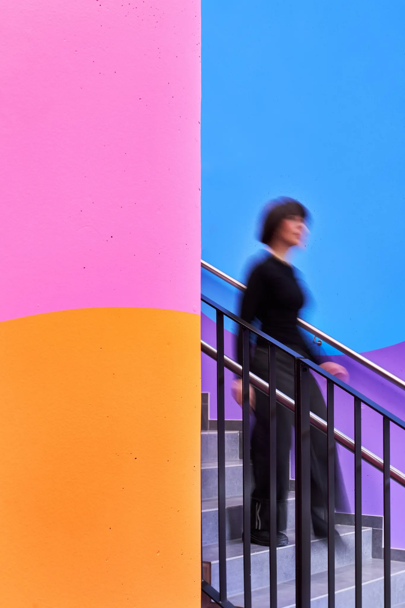 Person moving through a pink, orange, blue and purple stairwell